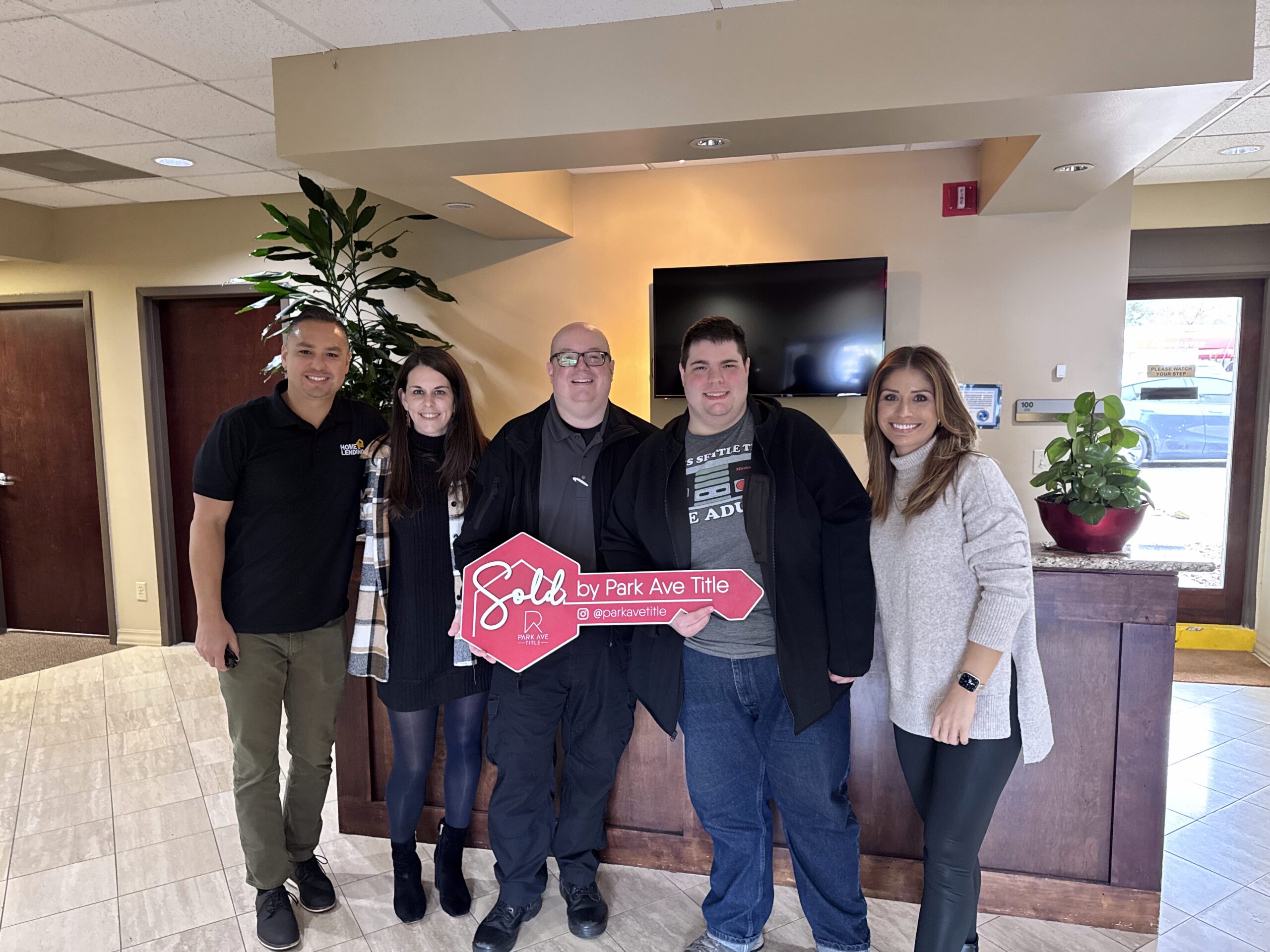 Jessica Remillard Smiling with Clients at Closing Day Jessica Remillard with Clients at Closing holding a sign that is a pink key
