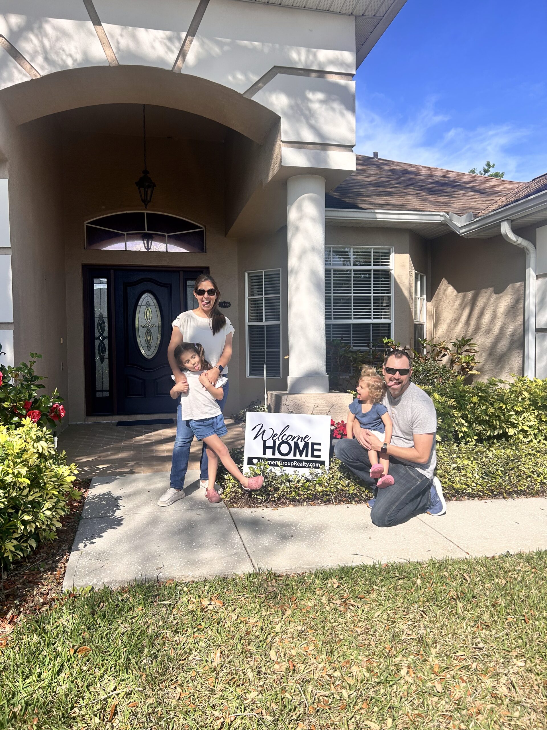 Jessica Remillard's Client's Family in front of their new home on closing day Jessica Remillard Clients at Closing in front of their new home with the welcome home sign.