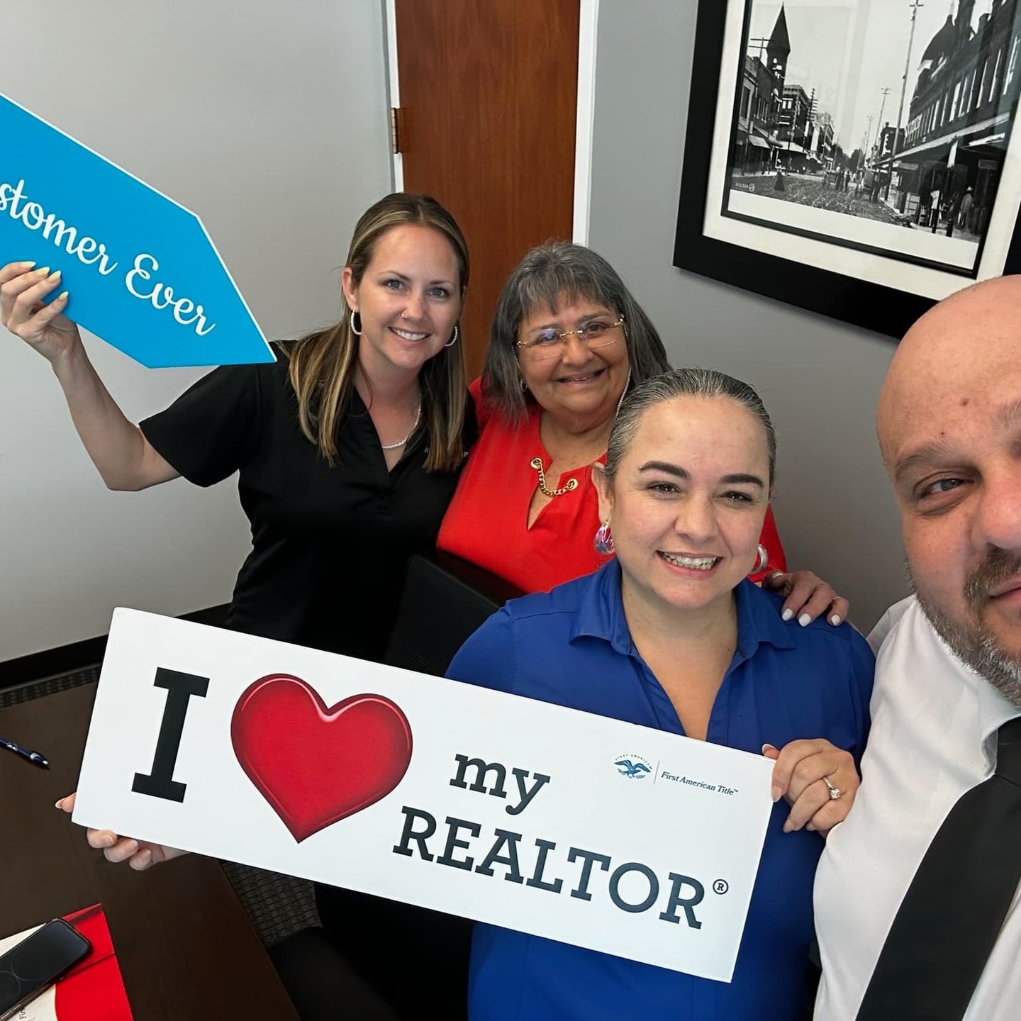 Tiffany Jolly stands with three clients in an office holding cheerful real estate signs, celebrating a successful closing together.